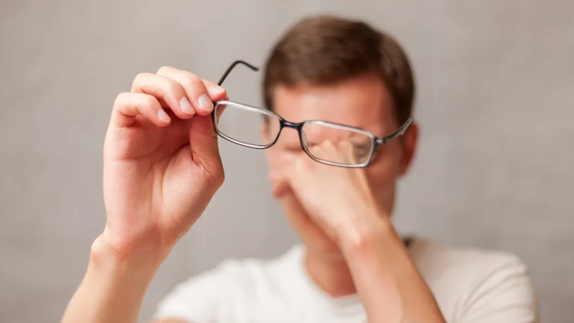 Hombre con vista borrosa por miopía sujetando sus gafas